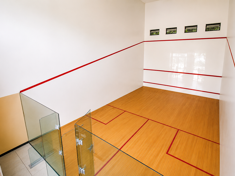 A well-maintained indoor squash court featuring professional timber flooring, glass viewing balustrade, and high-level clerestory windows for natural light.