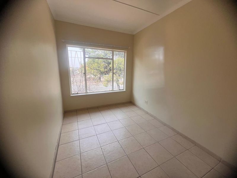A bright, empty bedroom featuring neutral tiled flooring and a large window fitted with security bars, offering a clean canvas for personalization.