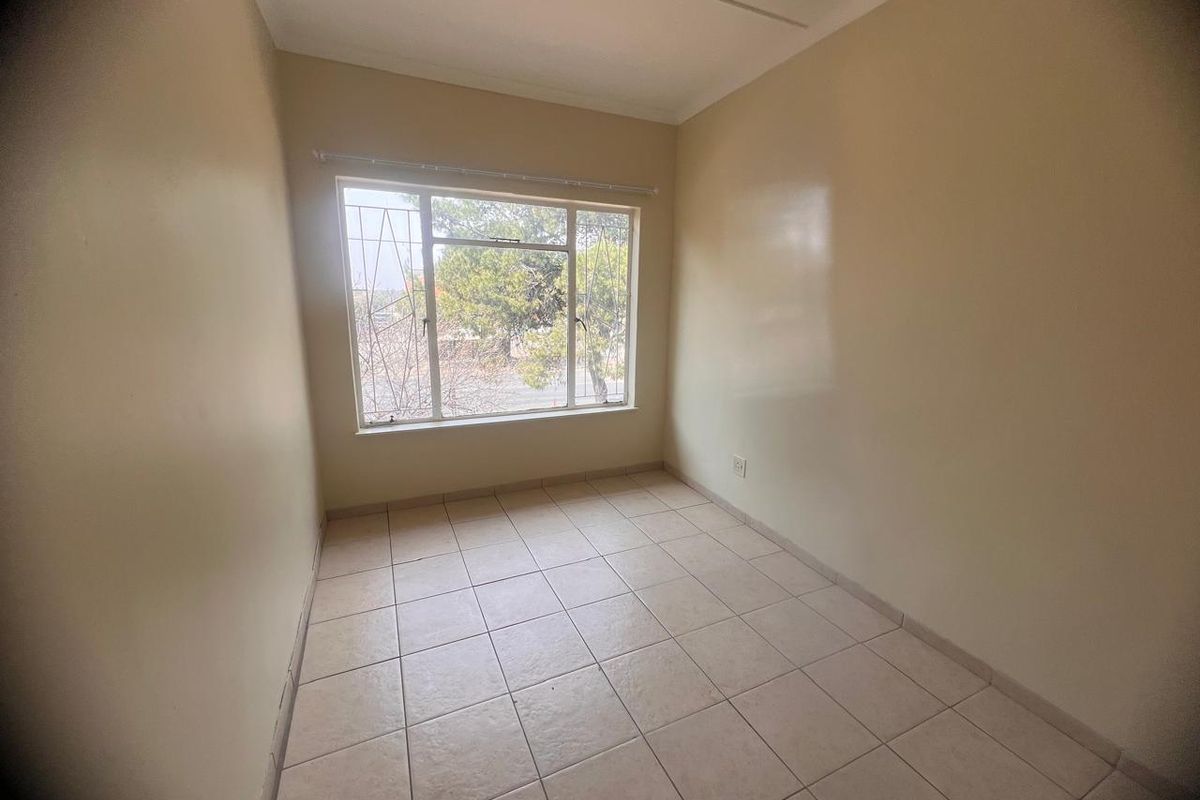 A bright, empty bedroom featuring neutral tiled flooring and a large window fitted with security bars, offering a clean canvas for personalization.