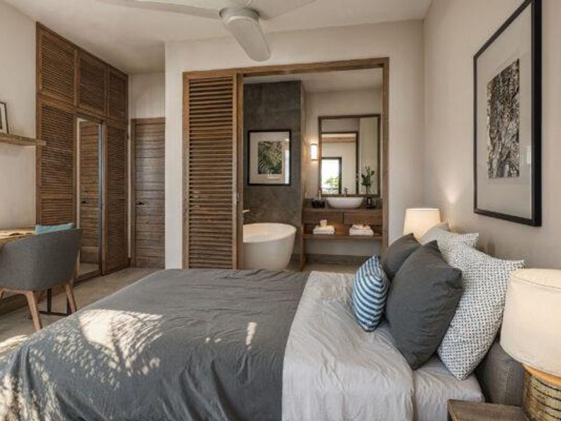 A well-appointed bedroom featuring built-in wooden louvered wardrobes and an open-plan ensuite bathroom with a freestanding bathtub and vanity.