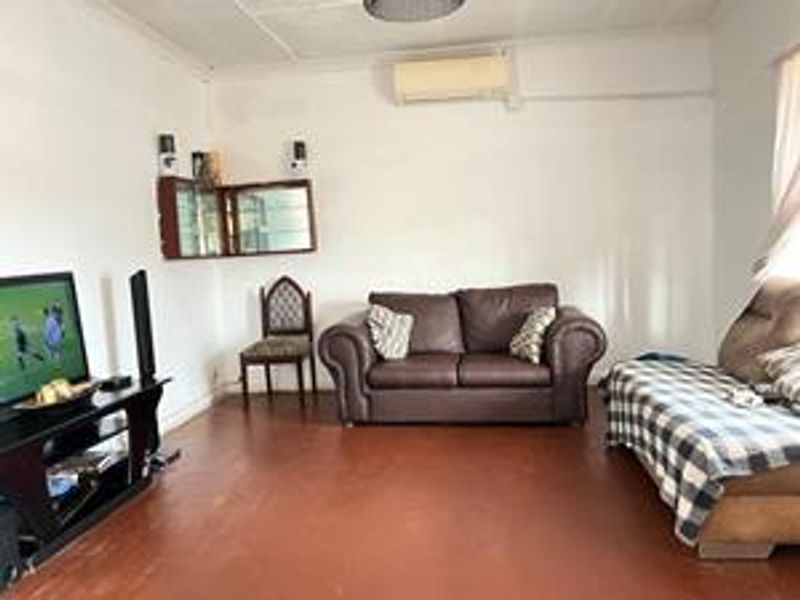 A living room featuring timber flooring, a wall-mounted air conditioning unit, and a built-in wall cabinet.