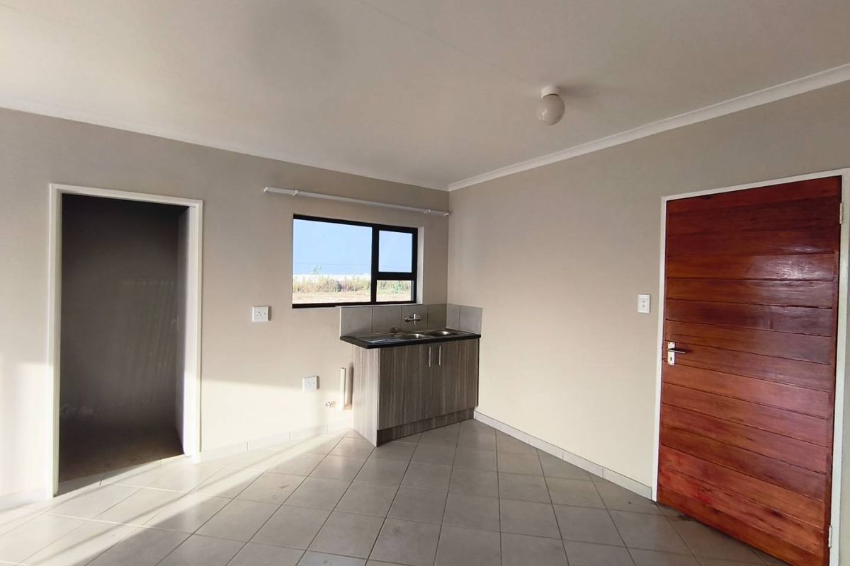 A compact kitchen area featuring a single sink unit with base cabinetry, tiled flooring, and a window providing natural light.