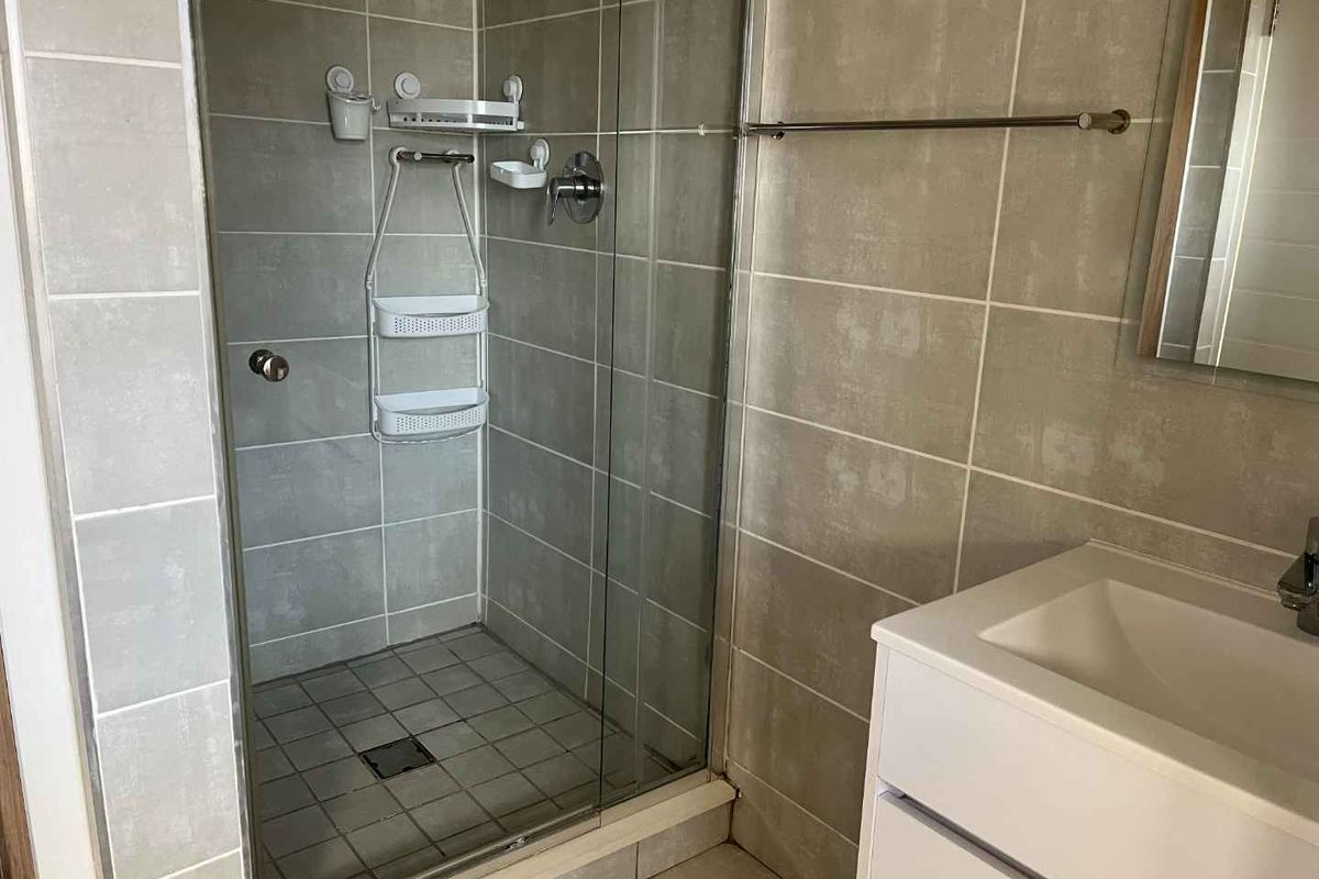 A clean bathroom featuring a glass-enclosed shower with grey wall tiles and a modern vanity unit with a basin.
