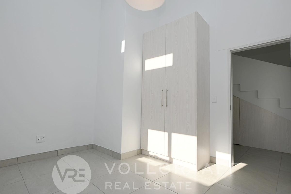 A bright, minimalist bedroom featuring neutral tiled flooring and a modern built-in wardrobe, offering a clean and versatile living space.