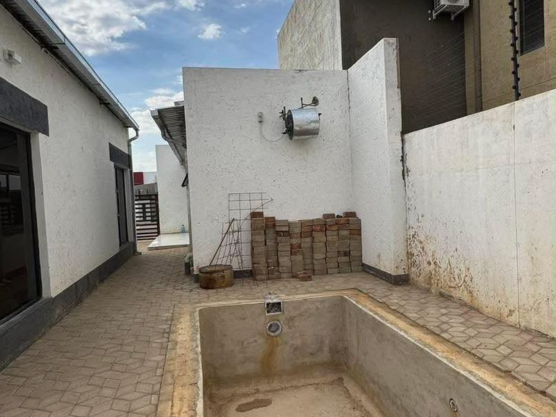 Outdoor pool area featuring a paved patio, boundary walls with electric fencing, and an empty, weathered swimming pool requiring maintenance and refurbishment.