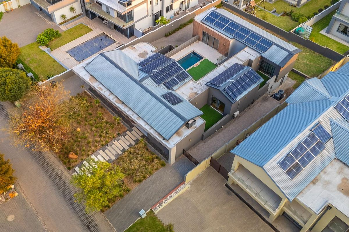 Aerial view of a modern residential property featuring extensive solar panel installations, a private swimming pool, and well-maintained landscaped garden areas.