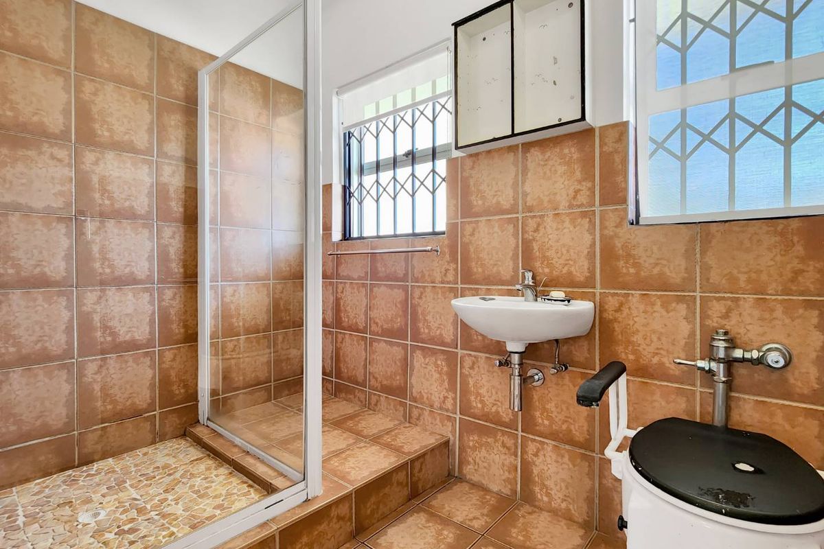 A functional bathroom featuring a walk-in shower with glass enclosure, wall-mounted basin, and toilet, finished with full-height brown ceramic wall tiles.