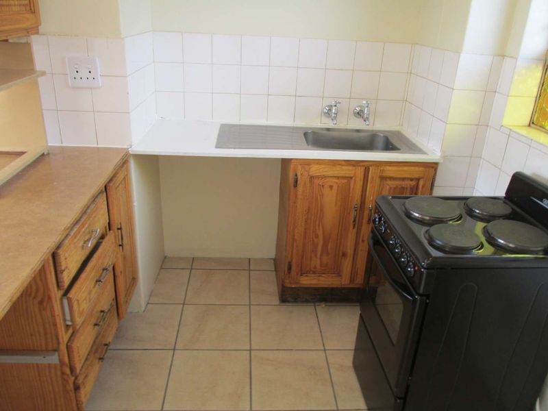 A functional kitchen area featuring wooden cabinetry, tiled splashbacks, a stainless steel sink, and tiled flooring, offering potential for modernization.