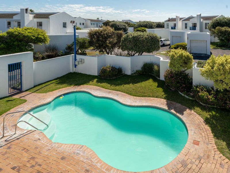 An elevated view of a private swimming pool with brick coping, surrounded by a well-maintained garden and secure boundary walls within a residential complex.