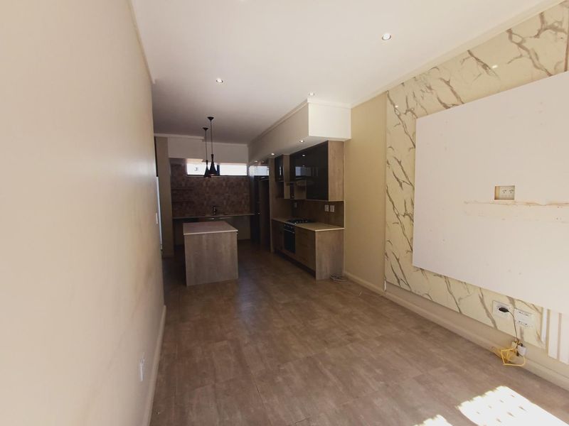 Open-plan living and kitchen area featuring modern cabinetry, a central island, and a decorative feature wall, offering a versatile space for living and dining.