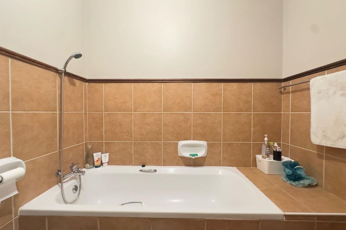 A bathroom featuring a built-in bathtub with a handheld shower mixer, tiled surround, and integrated soap dish.