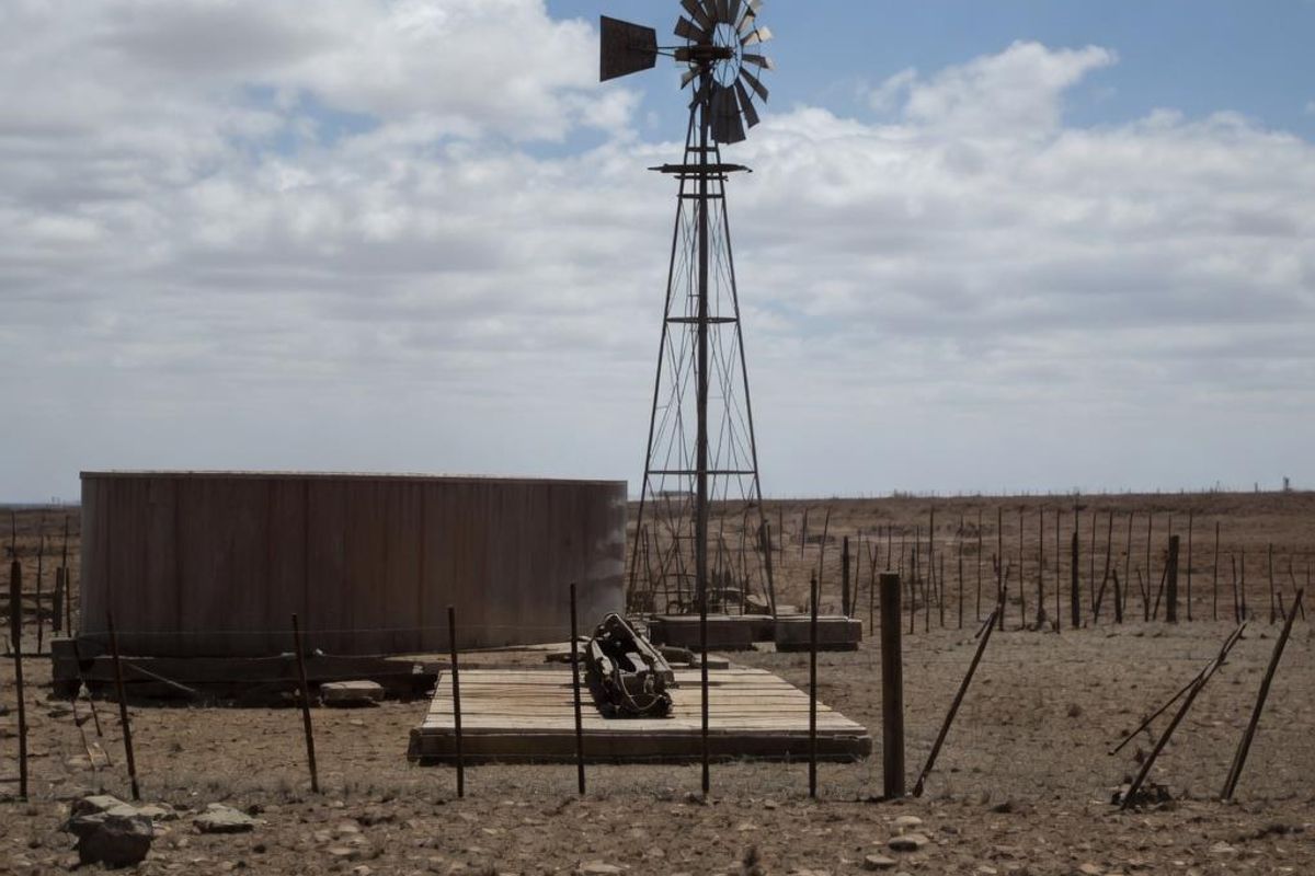 A rural farm landscape featuring a traditional metal windmill, a large water storage tank, and a wooden platform set within an open field.
