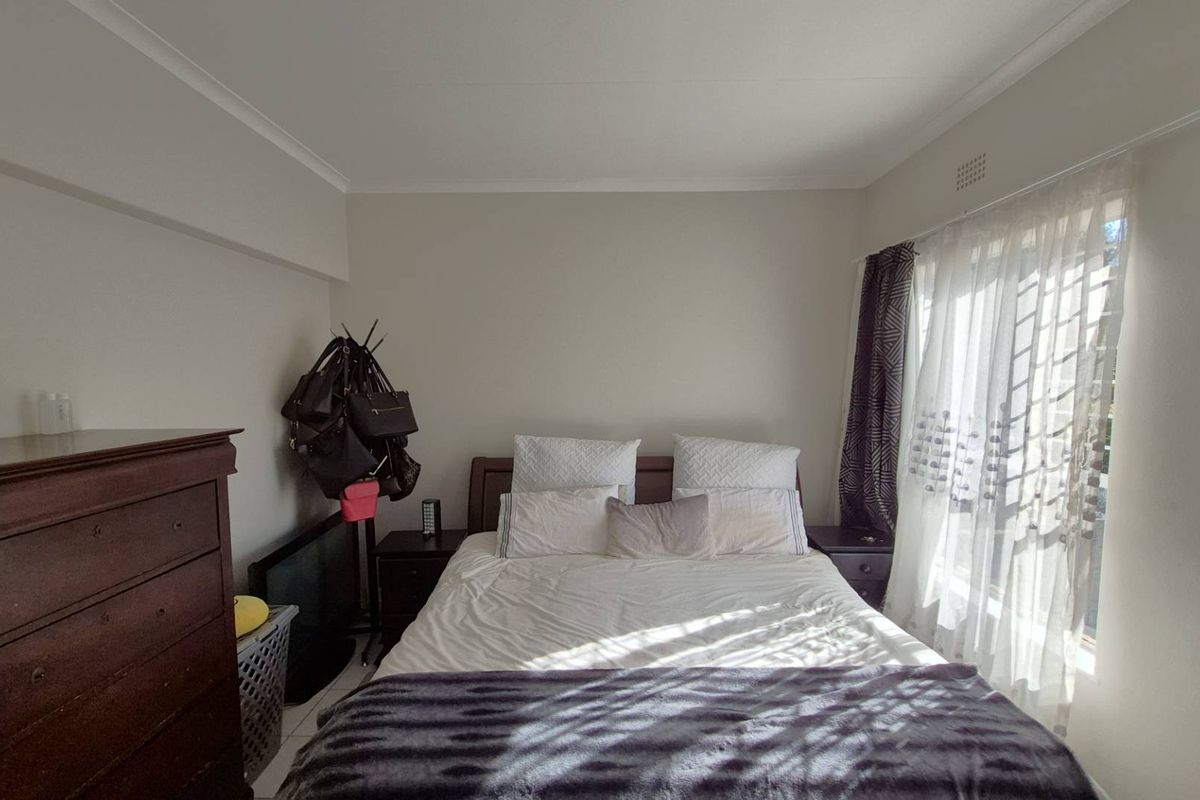 A well-lit bedroom featuring neutral wall tones, coved ceilings, and a large window with curtain tracks.