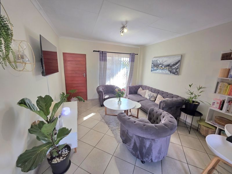 A well-maintained living room featuring neutral tiled flooring, a timber entrance door, and a security gate leading to the exterior.