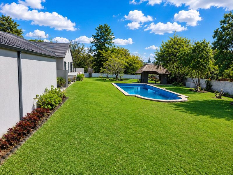 Spacious rear garden featuring a well-maintained swimming pool and a traditional thatched lapa, set within a private, landscaped outdoor area.