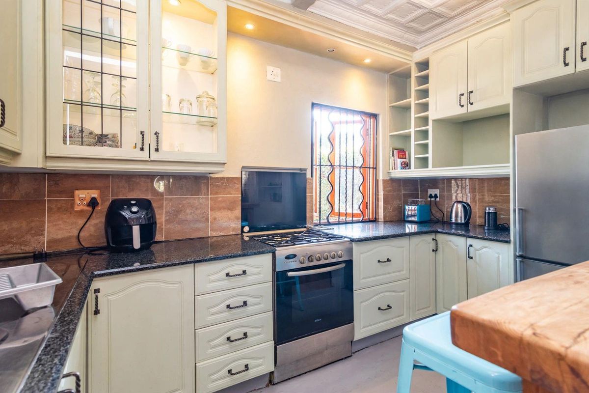 A well-maintained kitchen featuring light-toned cabinetry, granite countertops, a gas stove, and a tiled backsplash with integrated lighting.