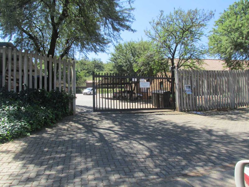 A secure gated entrance to the property featuring a paved driveway, perimeter fencing, and mature trees providing privacy.