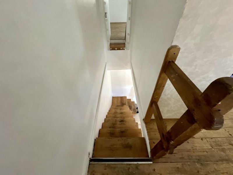 A narrow wooden staircase leading to a lower level, featuring exposed timber treads and a simple wooden handrail in a basic interior setting.
