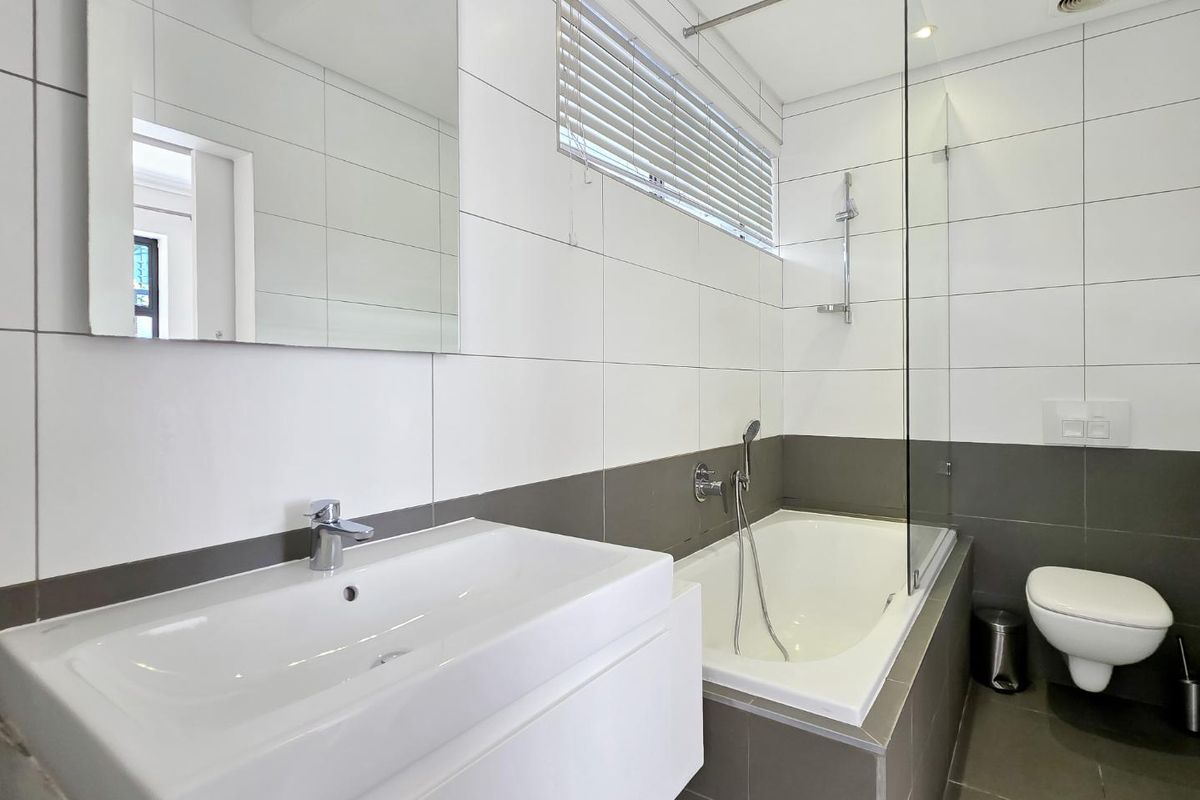 Modern bathroom featuring a wall-mounted vanity, built-in bathtub with glass screen, wall-hung toilet, and neutral tiled finishes.