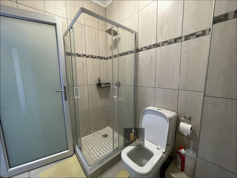 A compact, modern bathroom featuring a glass-enclosed shower, tiled walls, and a standard toilet, finished with a frosted glass door.