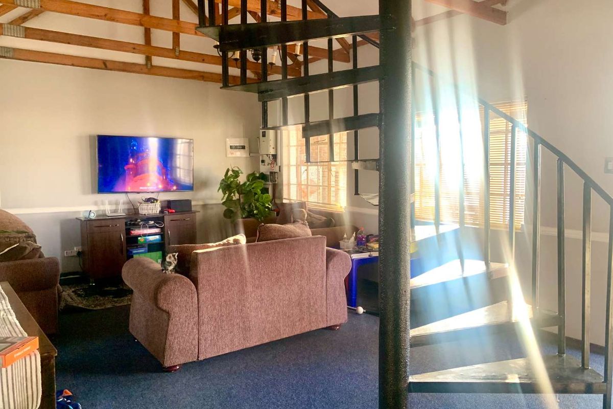 Spacious living area featuring a prominent black metal spiral staircase, exposed timber roof trusses, and large windows allowing for ample natural light.