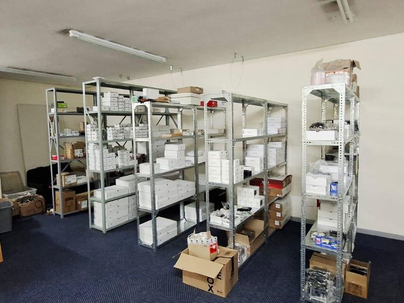 A functional utility or storage space featuring industrial metal shelving units, fluorescent overhead lighting, and carpeted flooring.