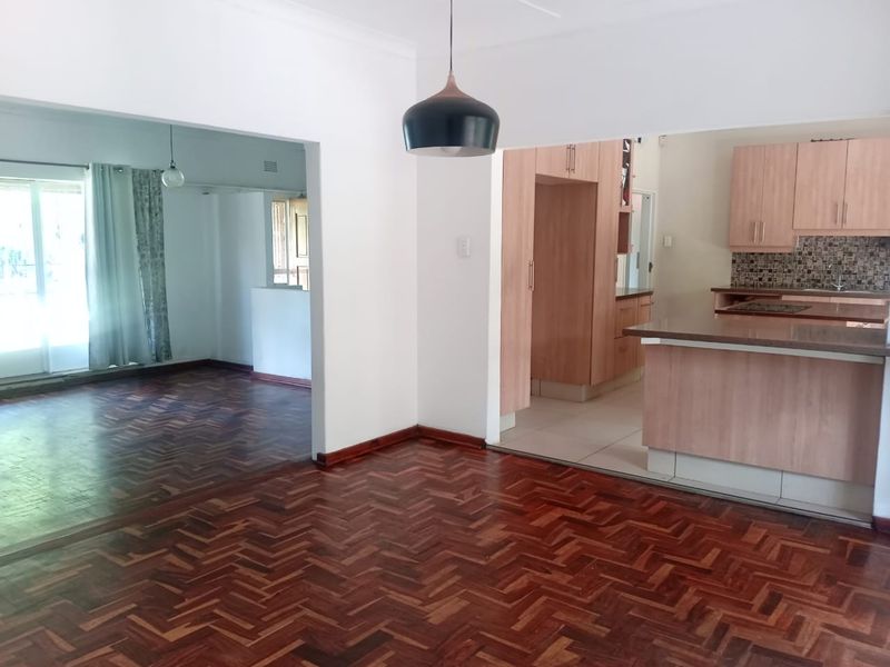 Spacious open-plan living and kitchen area featuring classic herringbone parquet flooring, modern cabinetry, and a functional breakfast bar layout.