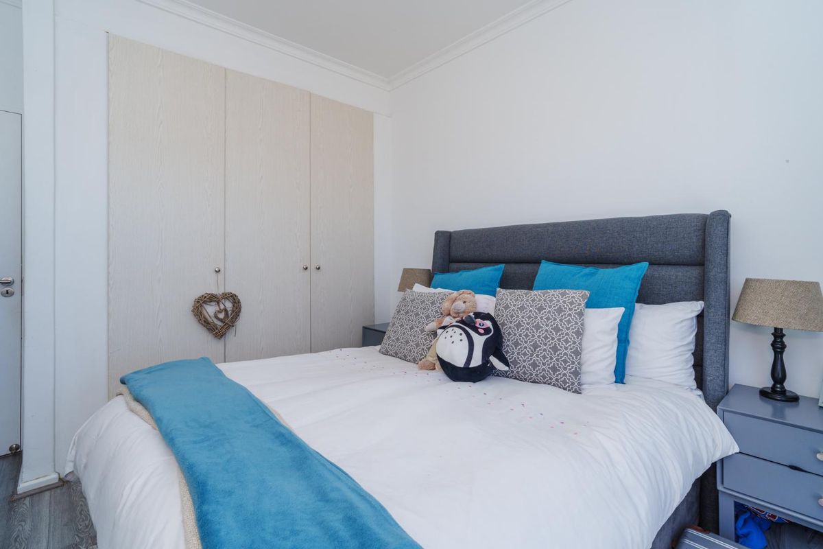A well-maintained bedroom featuring neutral built-in cupboards, coving details, and modern laminate flooring, providing a clean and functional living space.