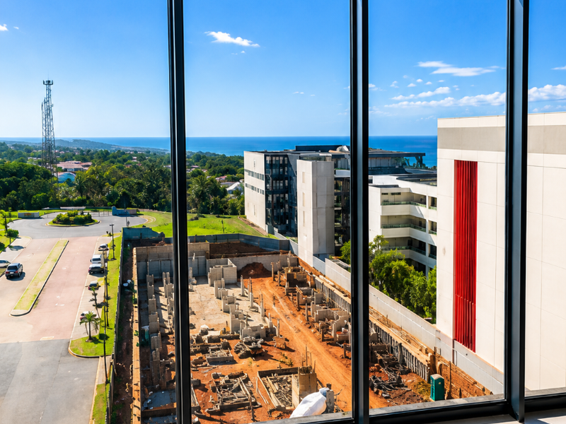 A bright, empty interior space featuring expansive floor-to-ceiling windows that offer a clear view of the surrounding neighborhood and distant coastline.