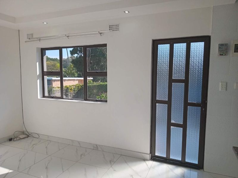 A bright, empty living area featuring modern marble-look floor tiles, recessed downlights, and a decorative patterned glass door leading outside.