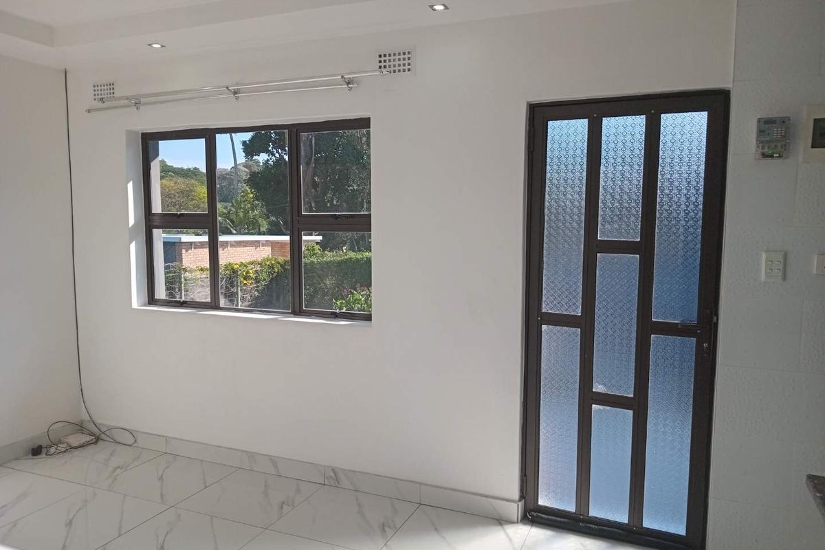 A bright, empty living area featuring modern marble-look floor tiles, recessed downlights, and a decorative patterned glass door leading outside.