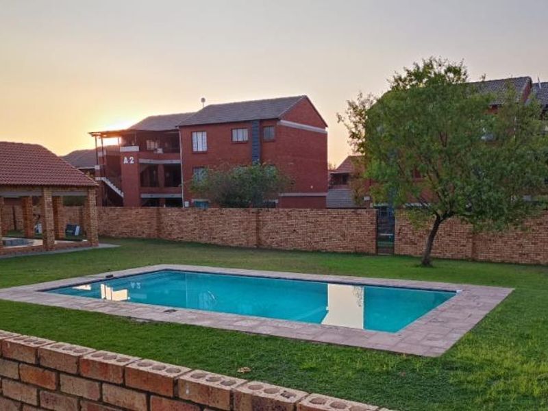 Communal outdoor area featuring a well-maintained swimming pool, paved surround, and a covered gazebo set within a landscaped garden.