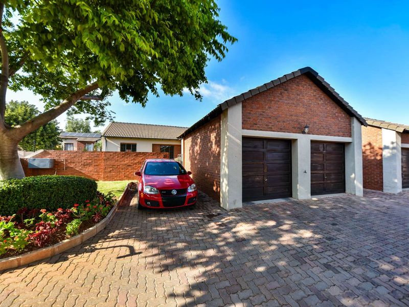 Front exterior view of a townhouse featuring a double garage with dark wooden doors, brick facade, and a paved driveway.