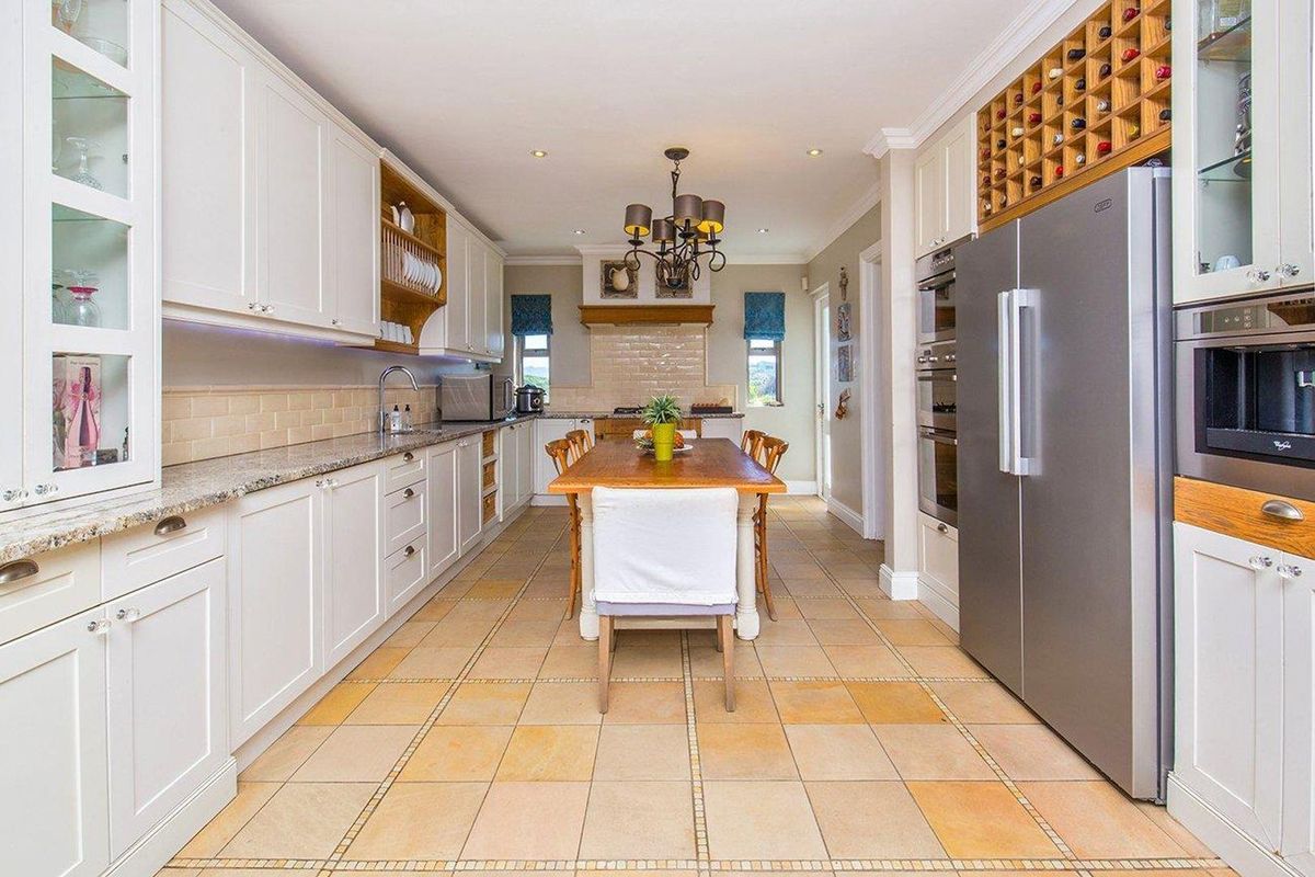 Spacious kitchen featuring white cabinetry, granite countertops, integrated wine rack, built-in oven, and tiled flooring with a central dining area.