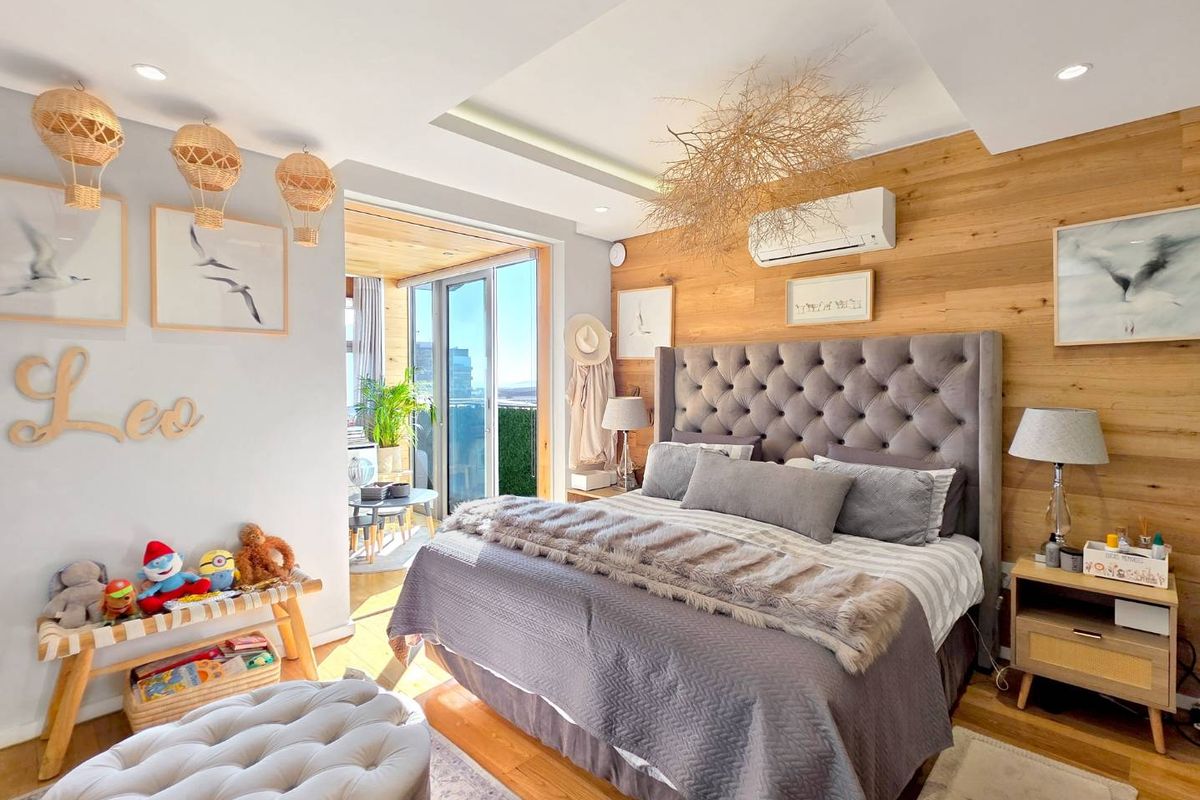 A well-appointed bedroom featuring wood-paneled accent wall, recessed ceiling lighting, split-system air conditioning, and direct access to a private balcony.