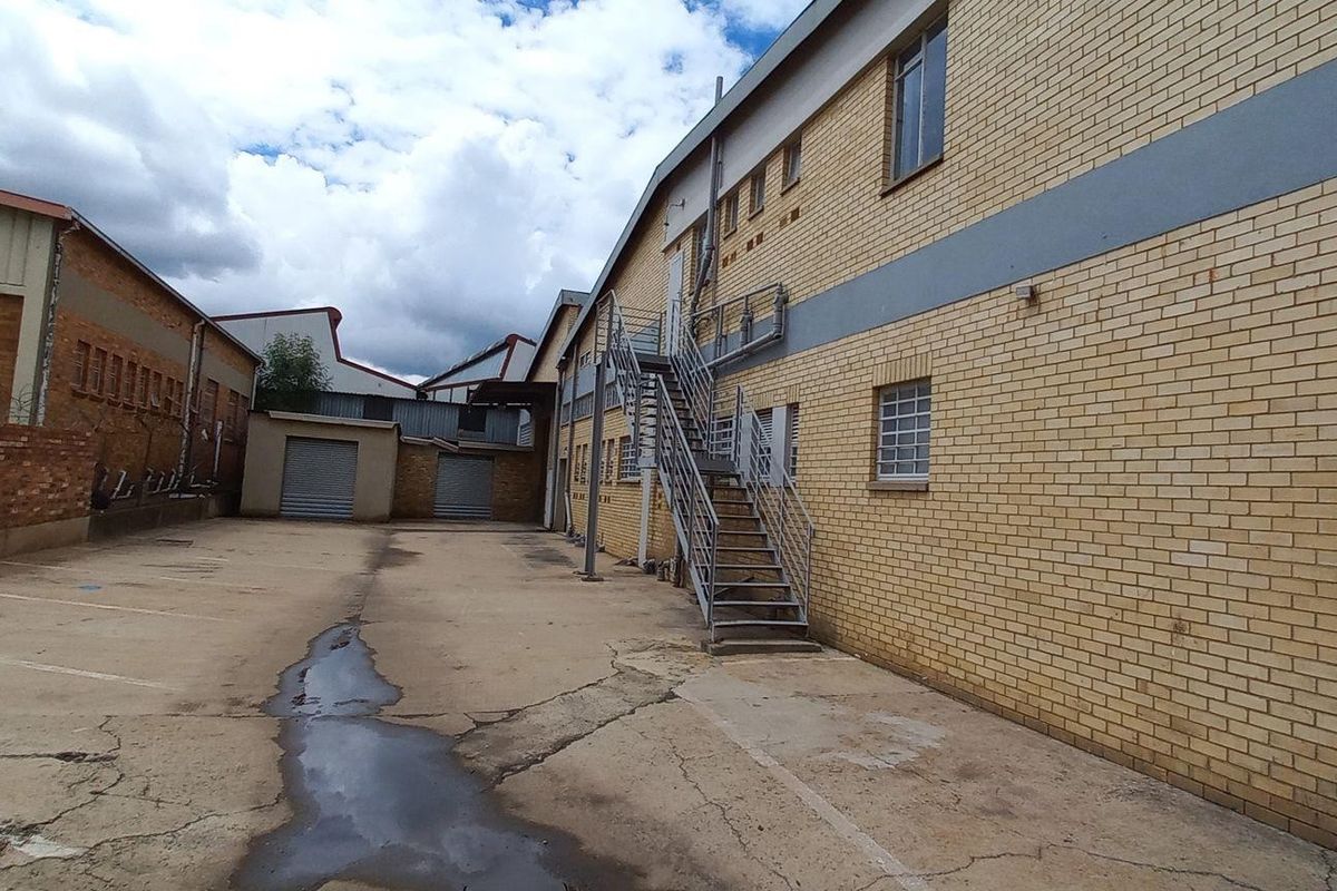 Exterior view of an industrial property featuring a paved yard, brick facade, and external metal staircase providing access to the upper level.