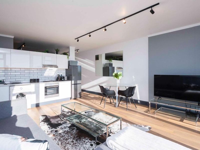 Modern open-plan living area featuring a sleek kitchen with subway tile backsplash, integrated appliances, and contemporary track lighting throughout the space.