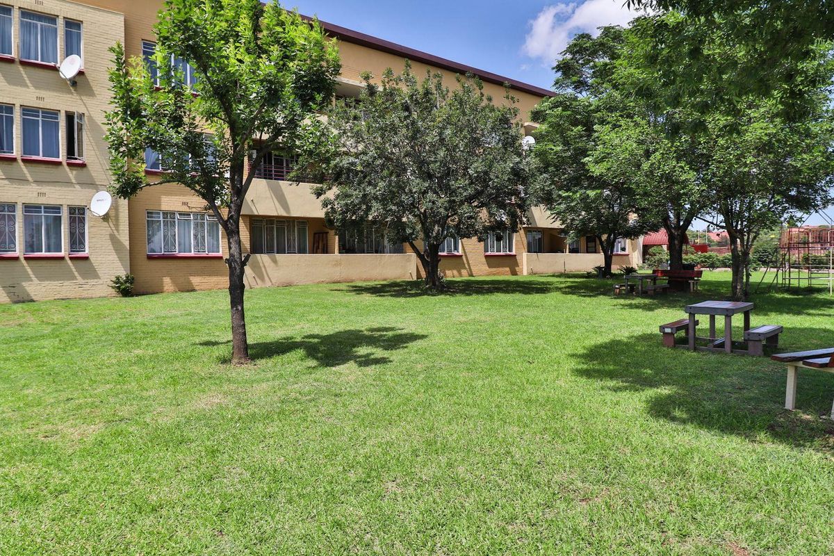 A view of the apartment complex exterior featuring a well-maintained communal lawn area with mature trees and paved pathways.