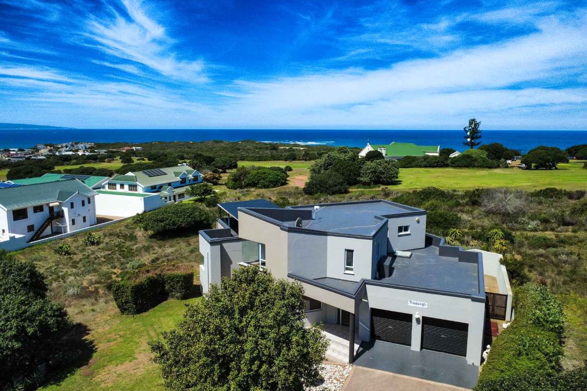 Aerial view of a modern multi-level coastal residence featuring a double garage, flat roof design, and scenic ocean views.