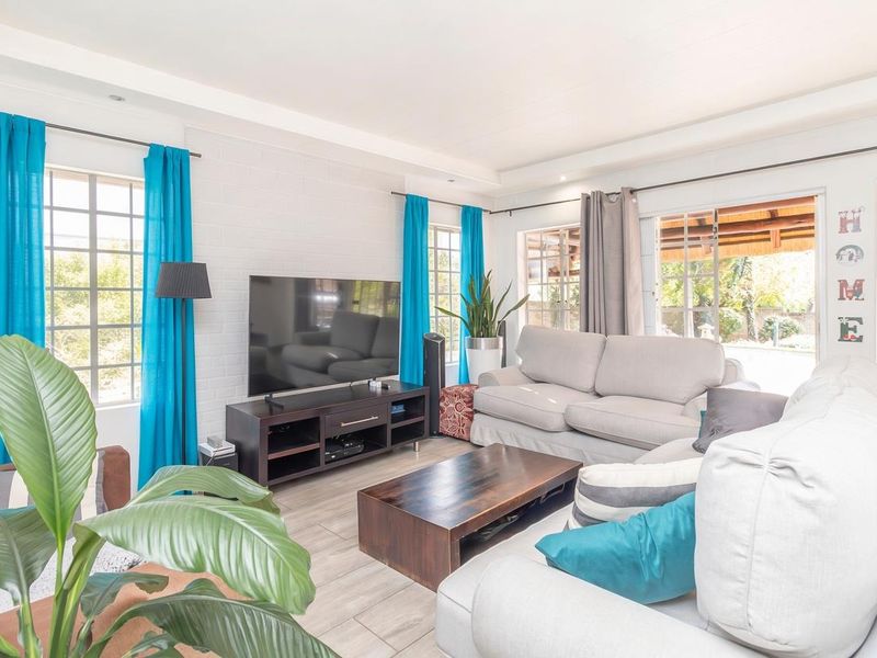 A bright and spacious living room featuring tiled floors, painted brick walls, and large windows that provide ample natural light and access to the patio.