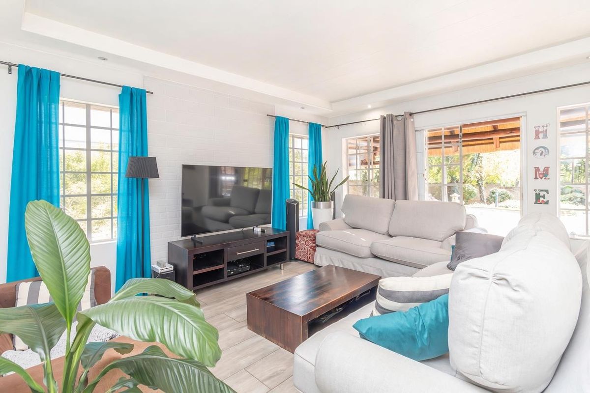 A bright and spacious living room featuring tiled floors, painted brick walls, and large windows that provide ample natural light and access to the patio.