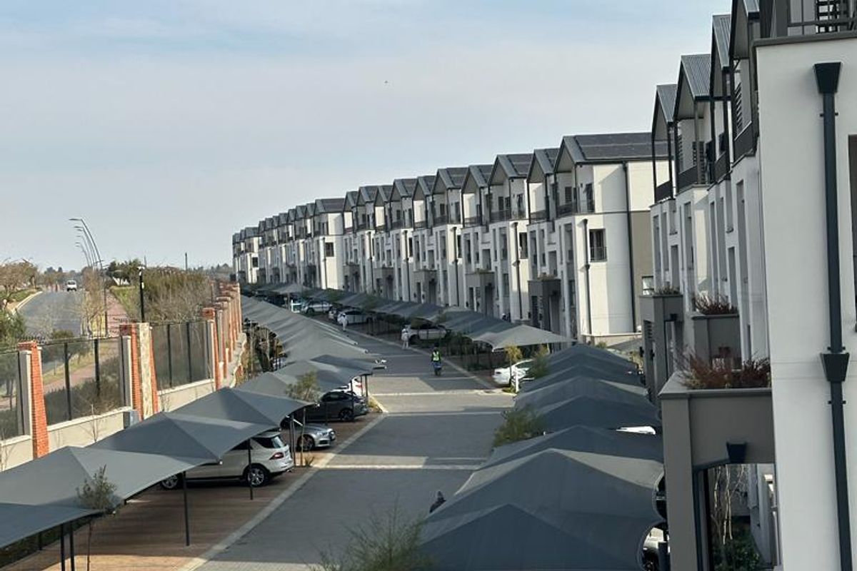 An elevated view of a modern apartment complex featuring a paved driveway with multiple shade cloth carports and contemporary building facades.