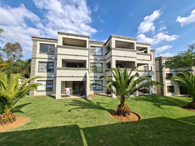 Rear elevation of a multi-story apartment complex featuring private balconies, aluminium window frames, and a well-maintained communal garden area.