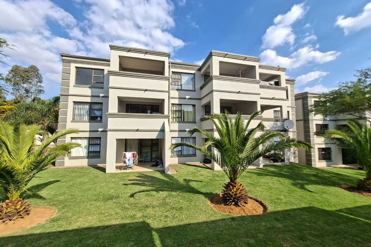 Rear elevation of a multi-story apartment complex featuring private balconies, aluminium window frames, and a well-maintained communal garden area.