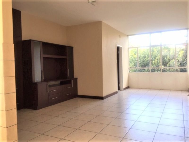 Spacious living area featuring neutral tiled flooring, large windows providing natural light, and built-in cabinetry for storage.