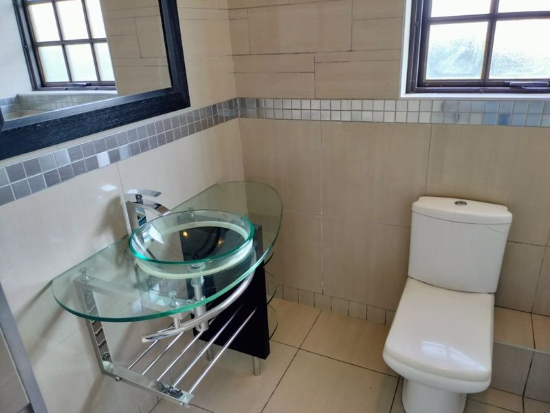 A modern bathroom featuring a glass vessel sink with a chrome faucet, a wall-mounted vanity, and neutral tiled walls with a decorative mosaic border.
