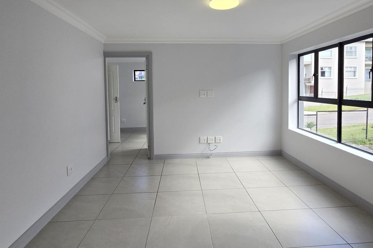 A bright, empty living room featuring neutral floor tiles, modern black-framed windows, and clean white walls, offering a versatile space for living or dining.