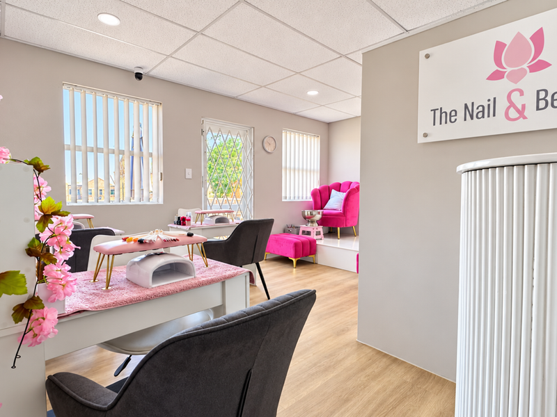 A well-maintained beauty salon space featuring laminate flooring, a suspended ceiling with recessed lighting, and large windows with vertical blinds.