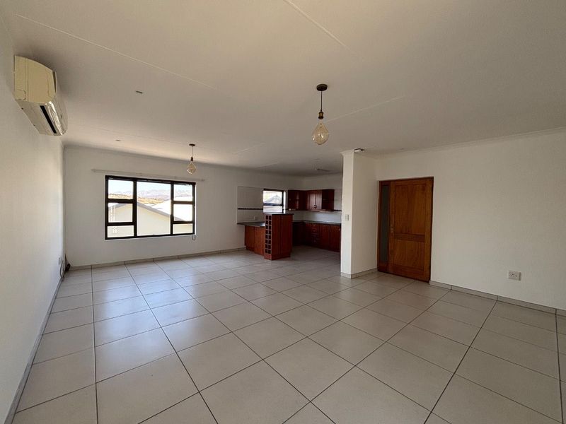 Spacious open-plan living area featuring tiled floors, a split-system air conditioner, and an integrated kitchen with wooden cabinetry.