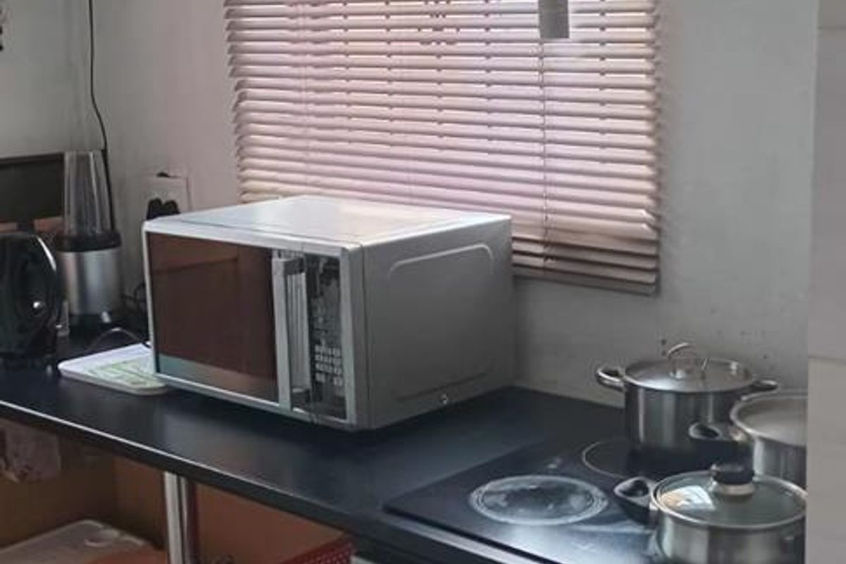 A compact kitchen area featuring a built-in electric oven, ceramic hob, and dark laminate countertop with a window providing natural light.